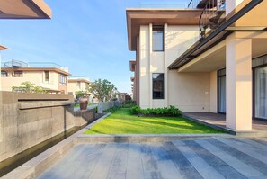 A modern residential building with a flat roof, a small garden area, and a paved walkway.