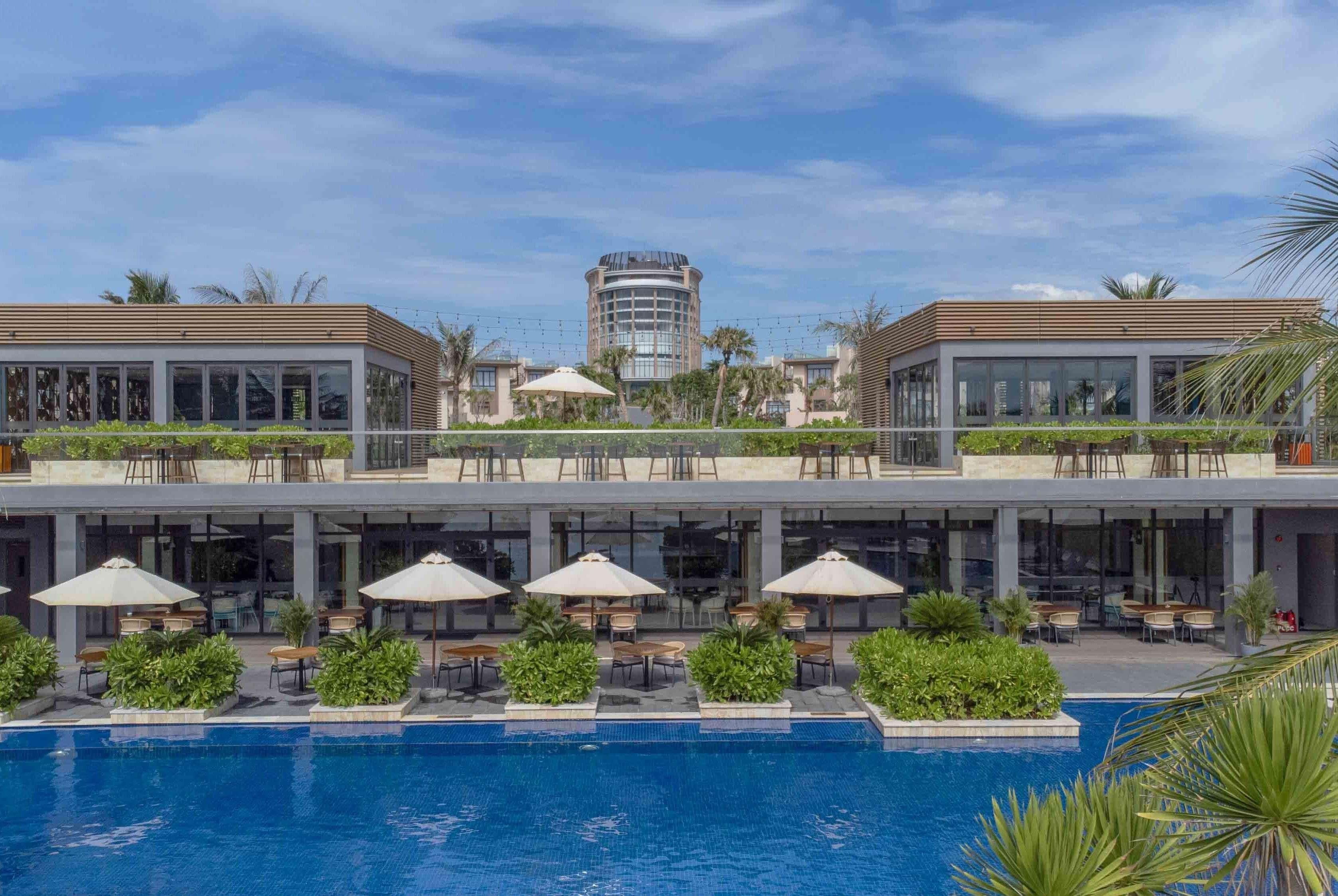 Ein Hotel mit Pool, Sitzgelegenheiten im Freien und Blick auf ein hohes Gebäude im Hintergrund.