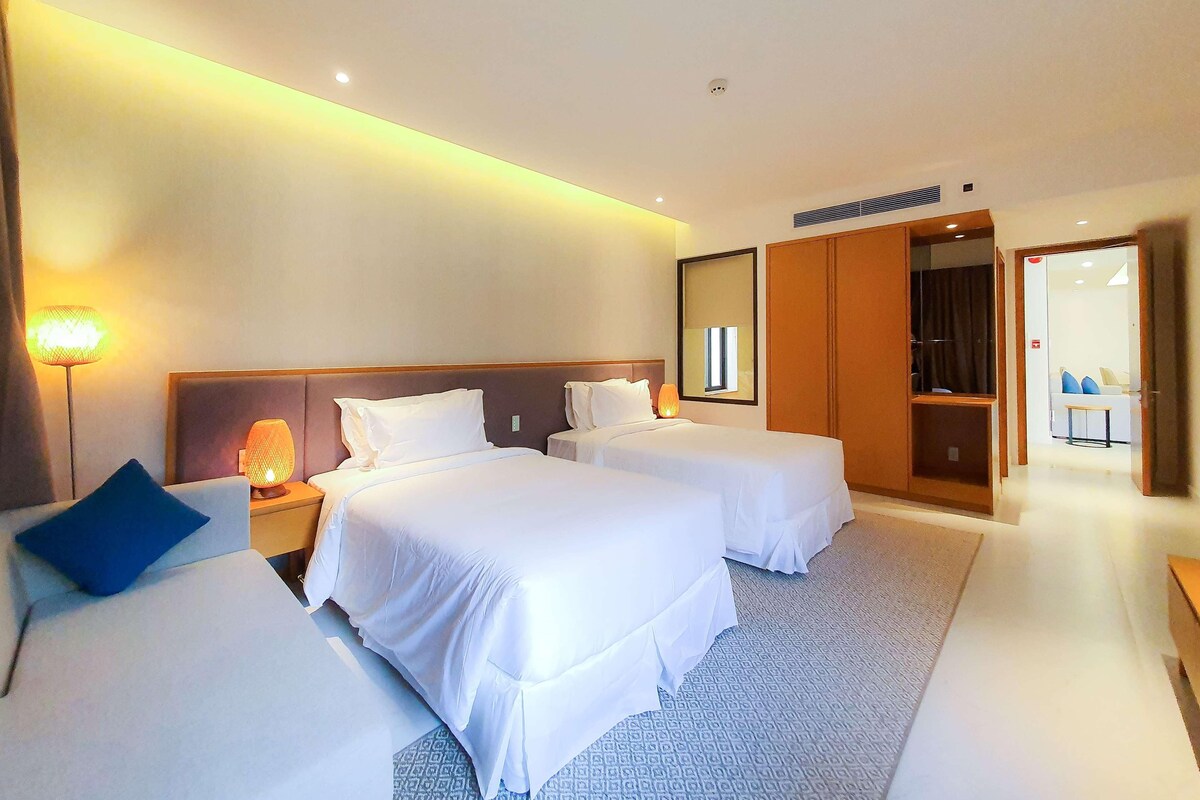 A hotel room with two beds, a nightstand with a lamp, a large mirror, and a wardrobe.