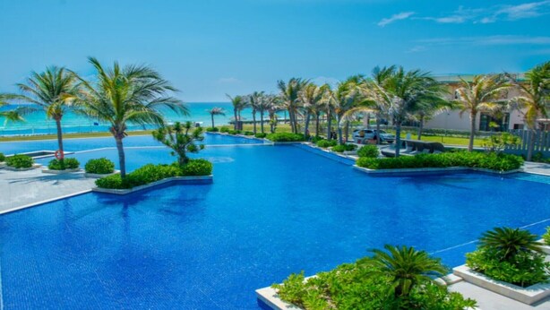 A large, clear blue swimming pool surrounded by palm trees and a view of the ocean. - Wyndham Garden Cam Ranh Resort (Cam Ranh)