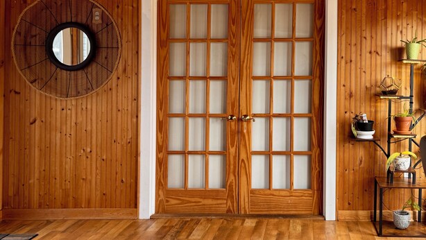 Een houten interieur met een traditionele schuifdeur, een ronde spiegel en een klein plantenplankje.