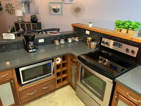 A kitchen with a built-in microwave, oven, and coffee maker. There are wooden cabinets and a black countertop.