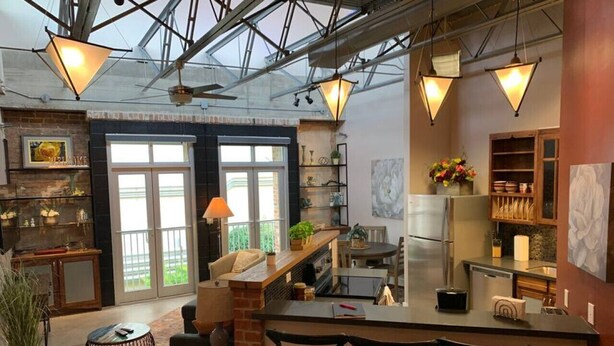 A modern kitchen with a central island, bar stools, and a dining area with a table and chairs. - Green Door Lofts-Waco Rose - Silos/Downtown (Waco)