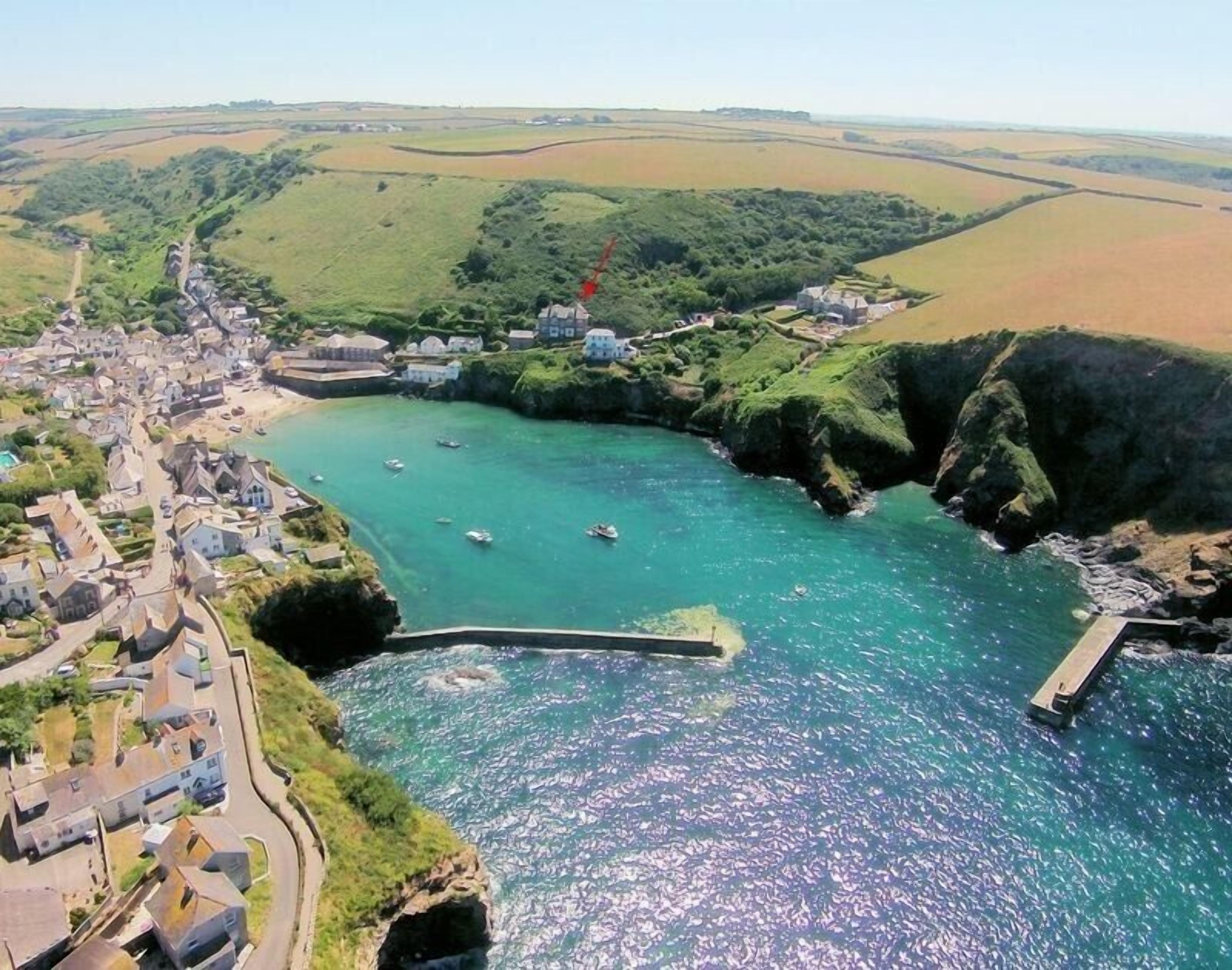 An aerial view of a coastal village with houses along the shoreline, a small harbor with boats, and a rocky coastline.