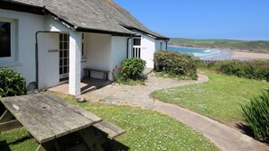 A white cottage with a stone pathway leading to a wooden bench and picnic table. - Gullsway: Sandpiper (Wadebridge)