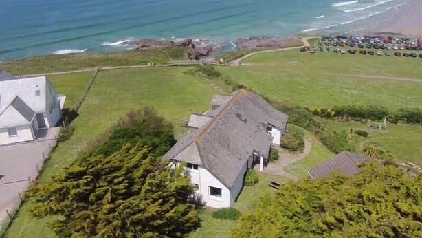 A coastal property with a grassy lawn, a house with a grey roof, and a beach with parked cars. - Gullsway: Sandpiper (Wadebridge)