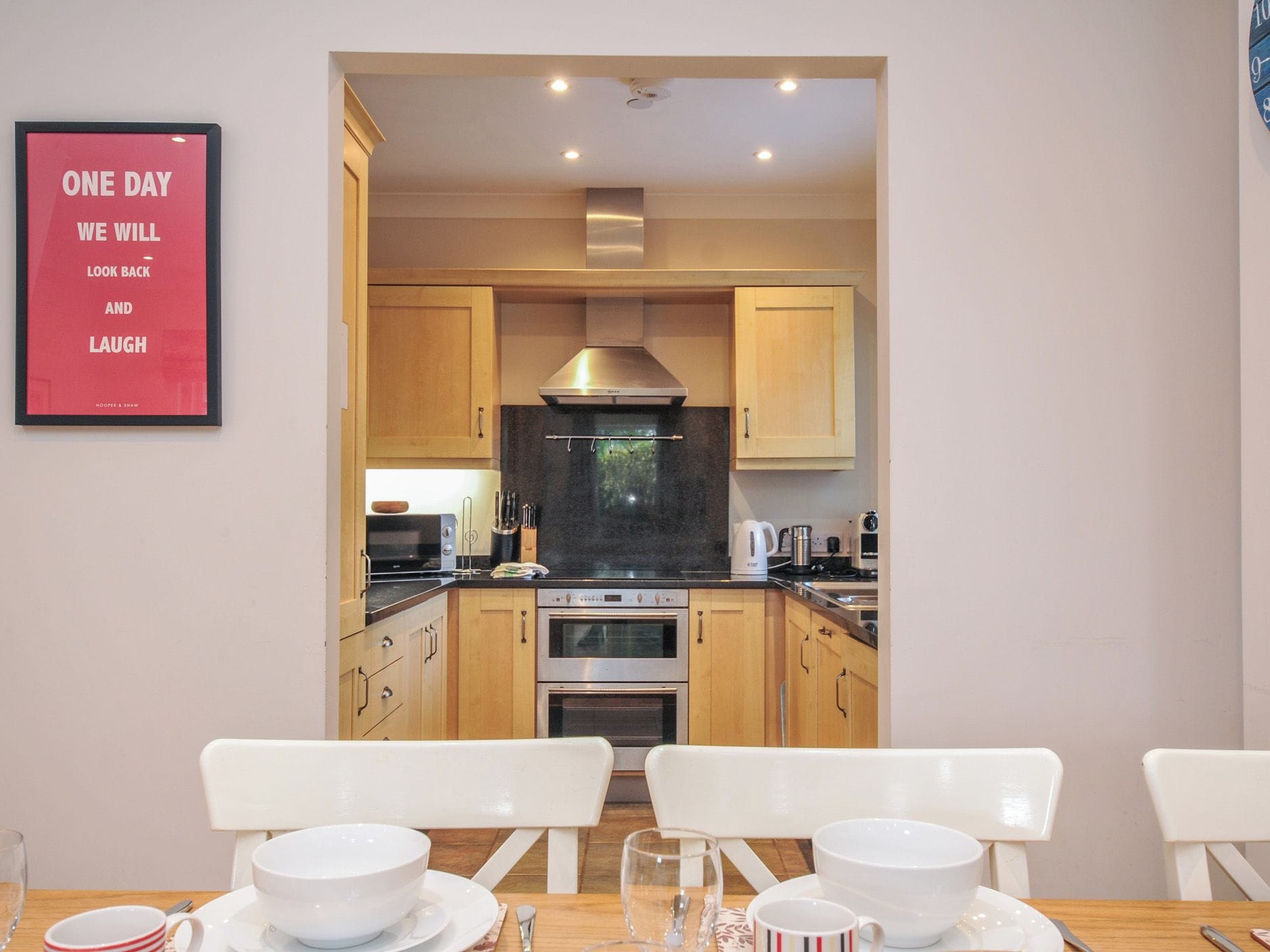 A modern kitchen with wooden cabinets, stainless steel appliances, and a dining area with white chairs and plates.