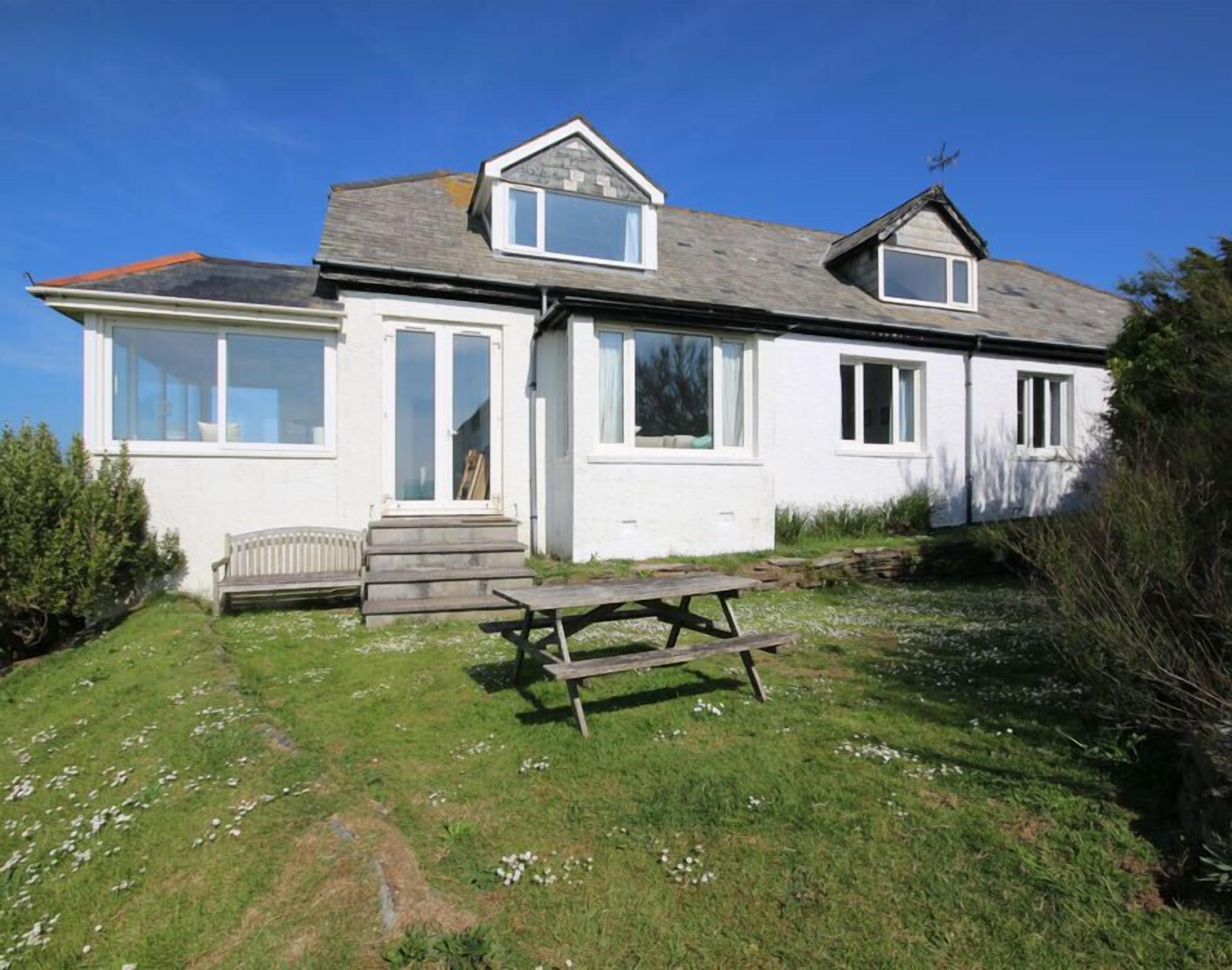 Een huis met twee verdiepingen, voorzien van een brede veranda, een houten bank en een picknicktafel.