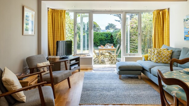 A living room with a sofa, armchairs, a TV, and a dining table with yellow curtains. - Lowenna Manor 4 (Wadebridge)