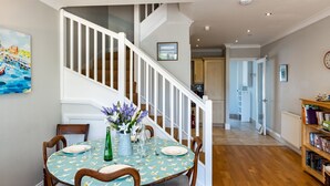 A dining area with a round table set for four, surrounded by wooden chairs. A staircase with white railings leads to an upper level. - Lowenna Manor 4 (Wadebridge)