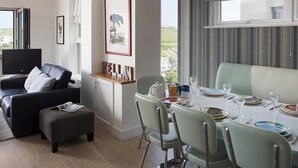 Una sala de estar moderna con un sofá, un reposapiés y un comedor con una mesa dispuesta para cuatro comensales.