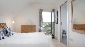 Un dormitorio con una cama grande, un aparador de madera y vistas al exterior a través de un ventanal.