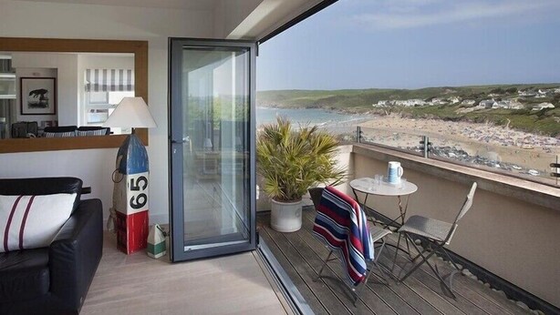 Un balcón con vista a la playa, un sofá, una mesa con sillas y una planta en maceta.