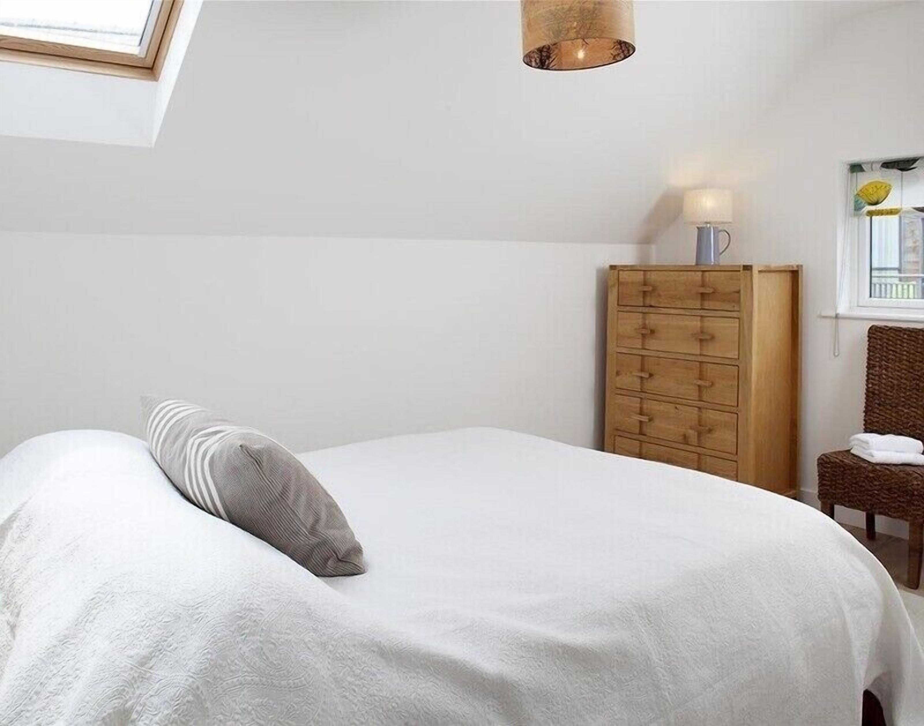 A bedroom with a bed, a wooden dresser, a chair, and a window with a view.