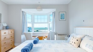 Un dormitorio con un ventanal grande, una cama con toallas azules, un aparador de madera y un radiador blanco.