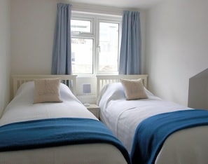 A bedroom with two single beds, a window with curtains, and a view of the outside.