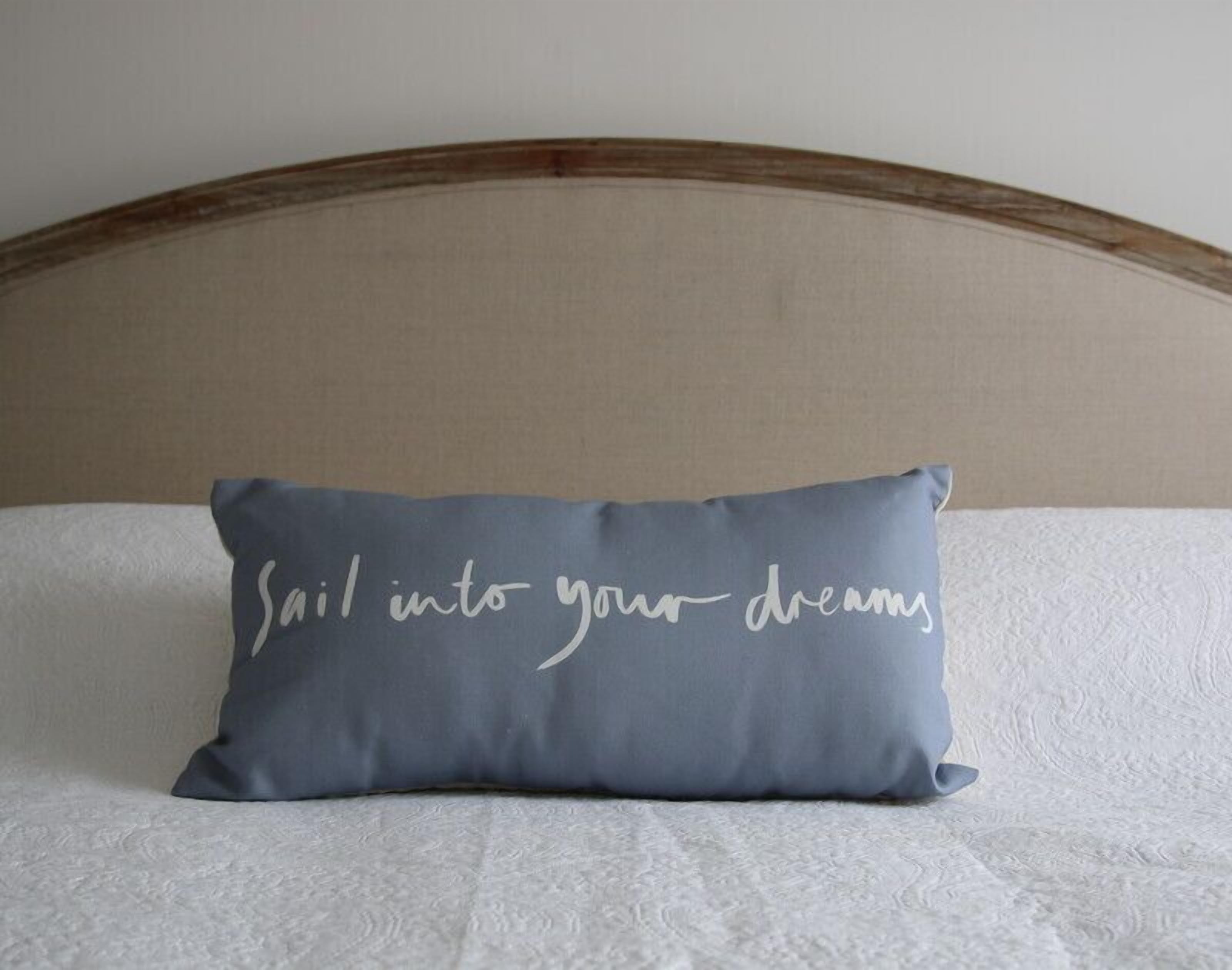 A bed with a pillow that has the text "Sail into your dreams" on it.