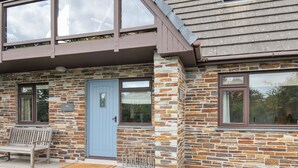 Een gebouw van natuursteen met twee verdiepingen, een blauwe deur, een houten bankje buiten en een houten terras.