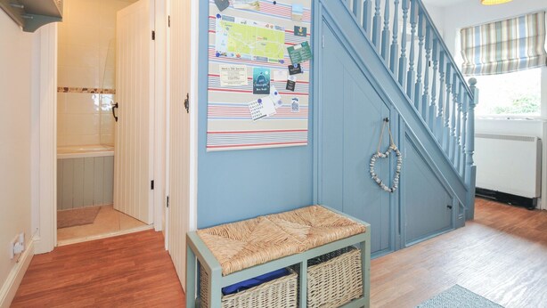 A staircase with blue railings, a wall-mounted map, and a bench with baskets. - Rocklings (Wadebridge)