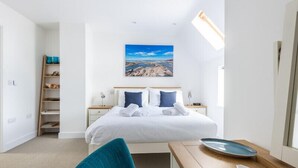 Habitación de hotel con una cama grande, un escritorio con silla, una estantería y un cuadro en la pared.