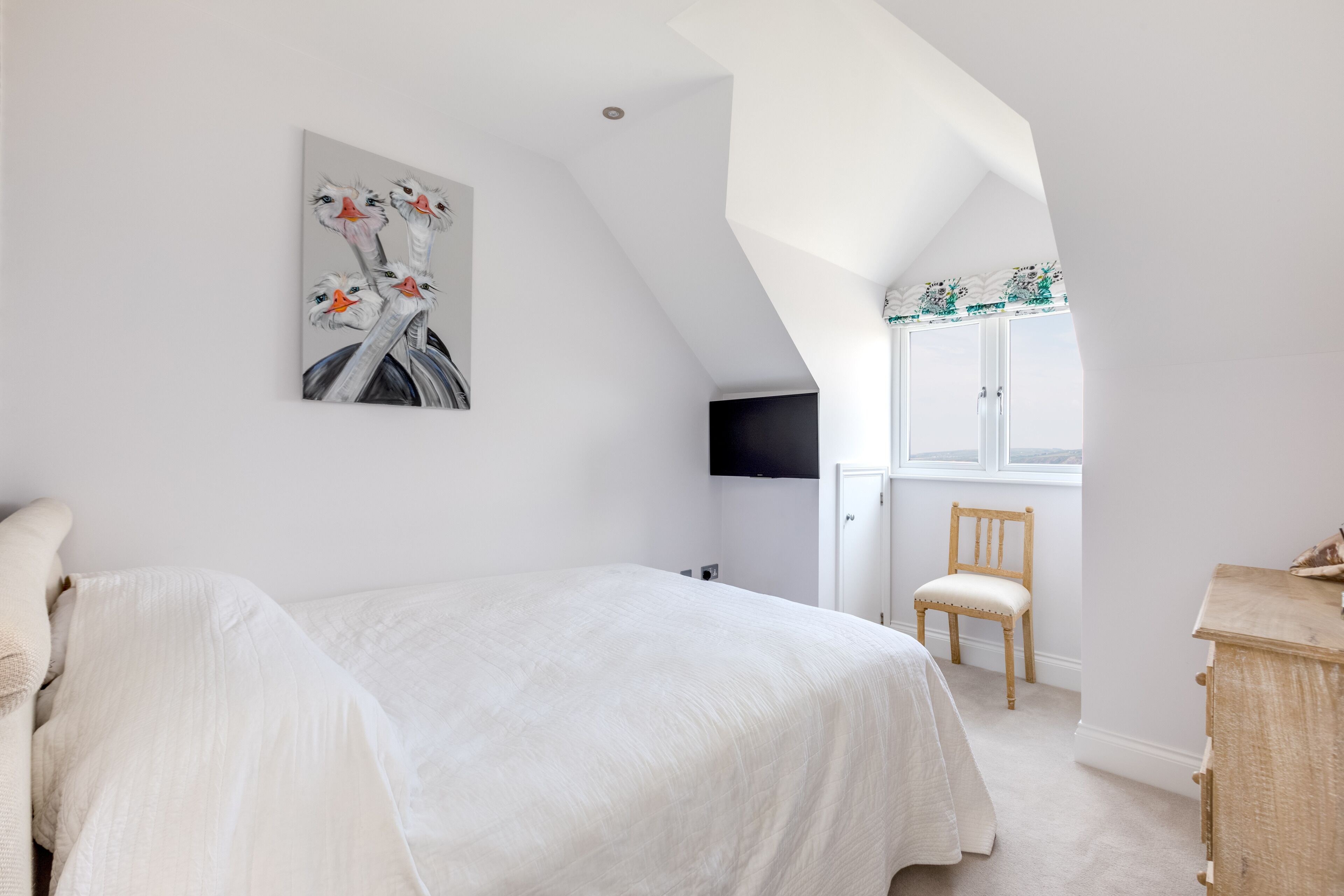 Une chambre avec un plafond en pente, un lit, une chaise, une commode et une fenêtre.