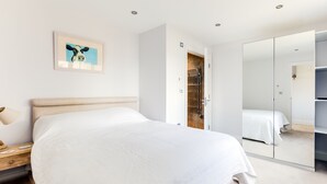 A modern bedroom with a large bed, a bedside table, a wall-mounted lamp, a framed artwork, and a wardrobe with a mirror. - Rock Lobster (Port Isaac)