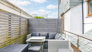 A patio area with a sofa set, a table, and a railing. - Rock Lobster (Port Isaac)