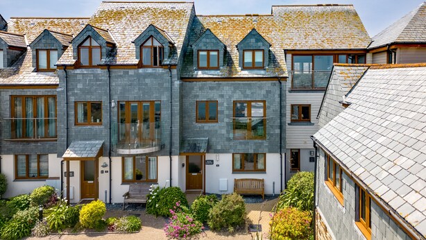A multi-story building with a stone facade, multiple windows, and a small garden area with various plants. - Rock Lobster (Port Isaac)