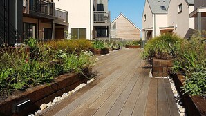 Een houten terras dat leidt naar een rij moderne gebouwen met balkons en een heldere lucht.