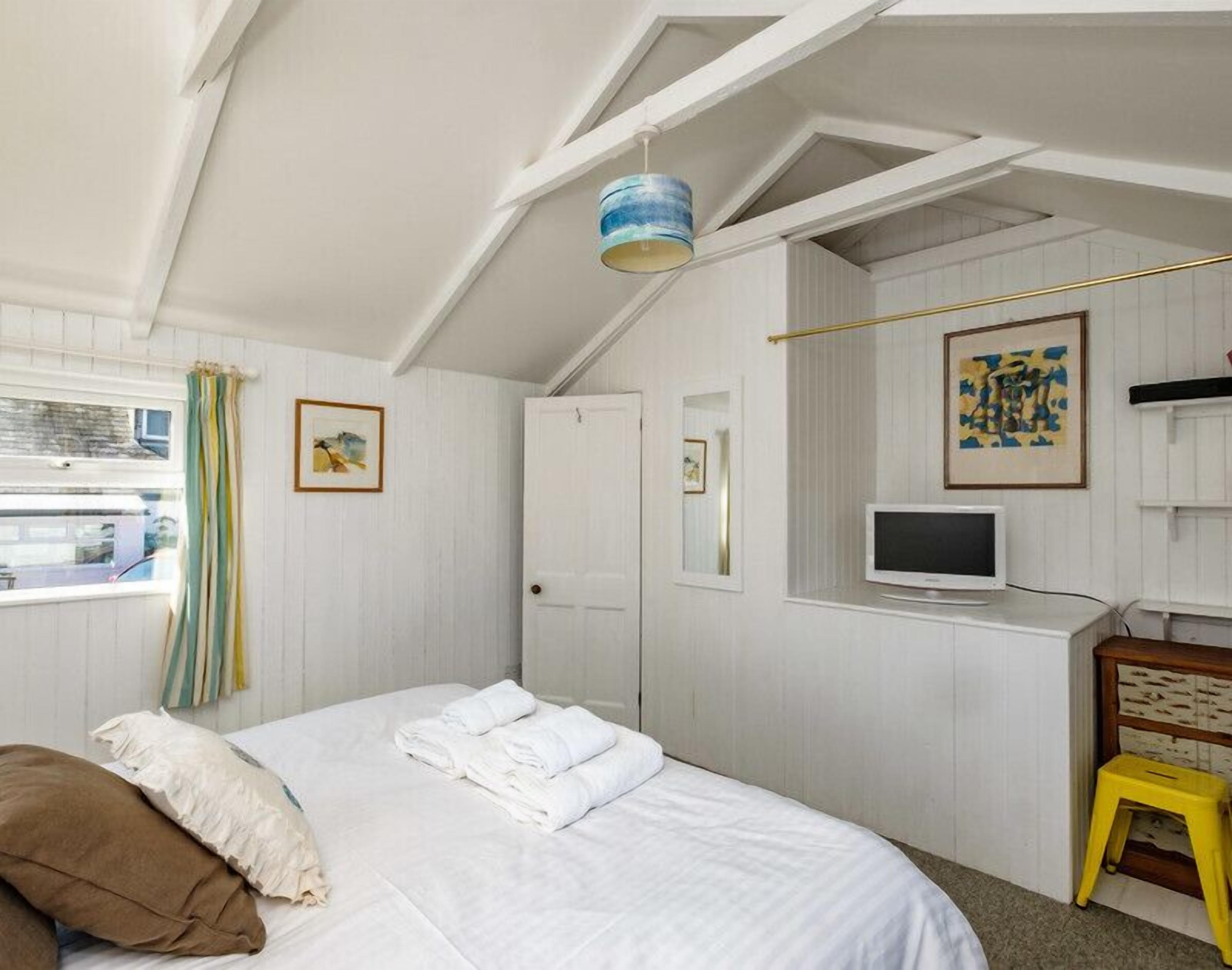 Um quarto com uma cama, televisão, janela com cortinas e uma porta.