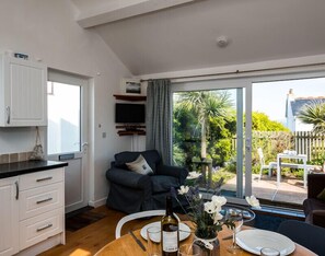 A modern kitchen with white cabinets, a dining area with a table set for two, and a large sliding glass door leading to a patio with a view of the sea.