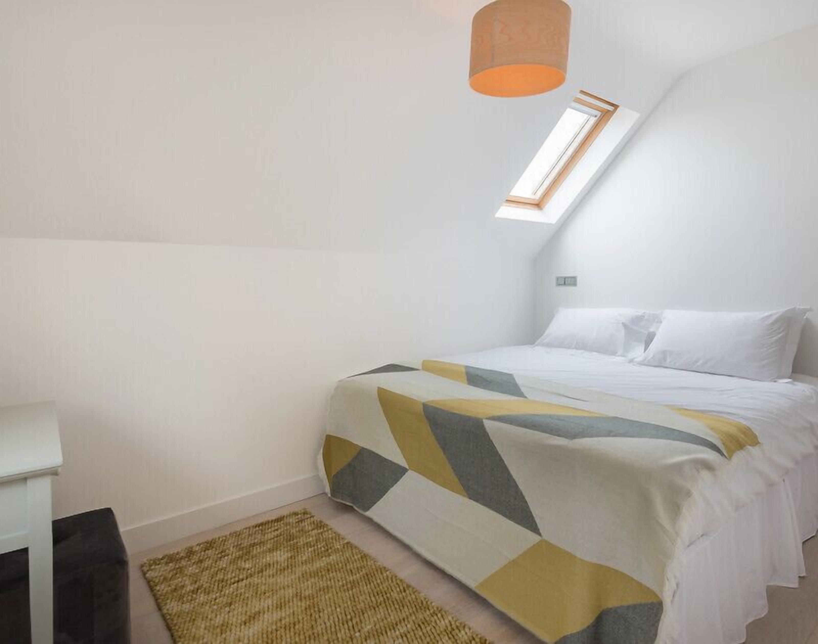 Et soveværelse med seng, et lille skrivebord, et vindue og en loftlampe.