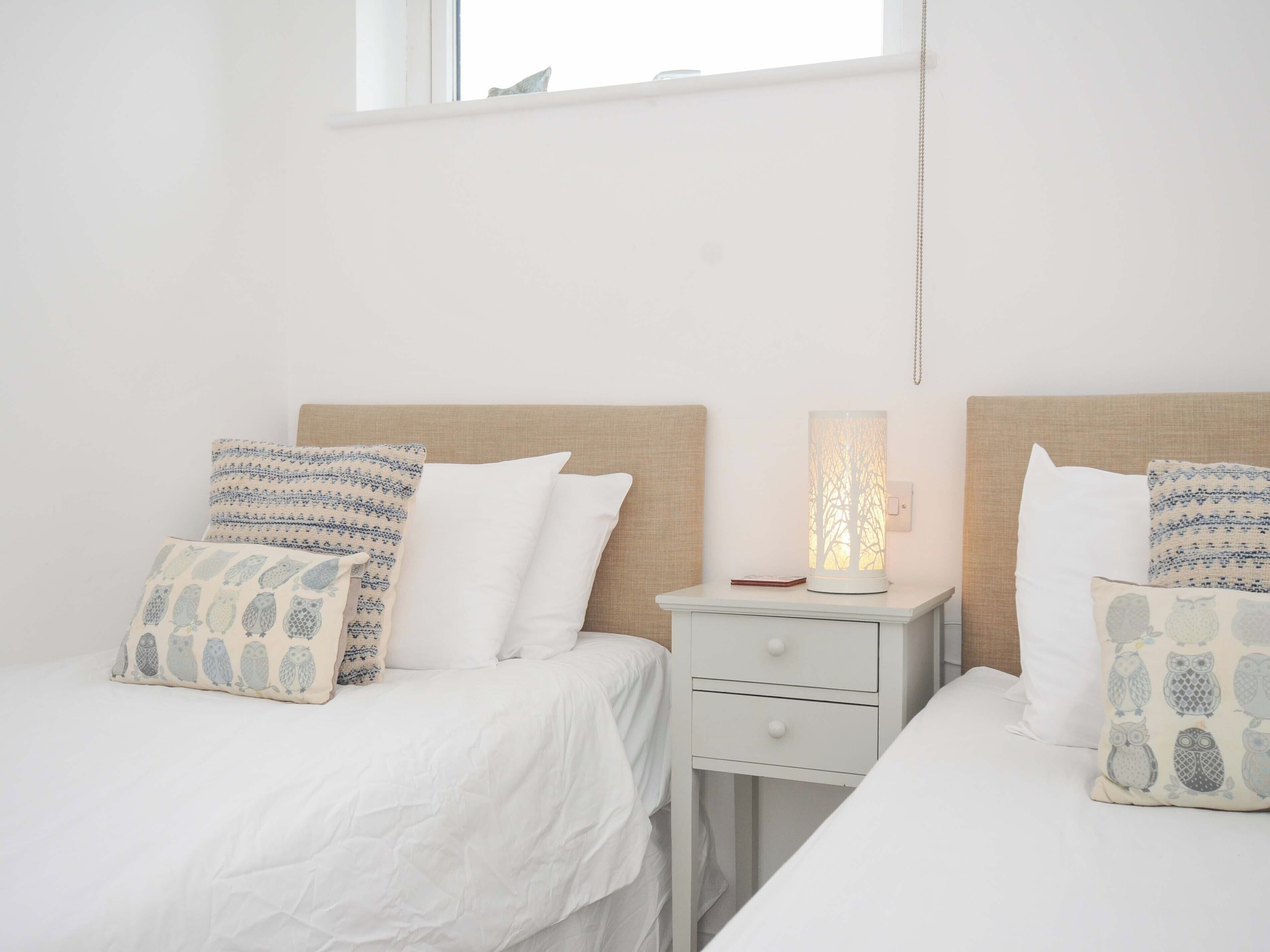 A bedroom with two beds, each with a headboard, a bedside table, and a lamp.