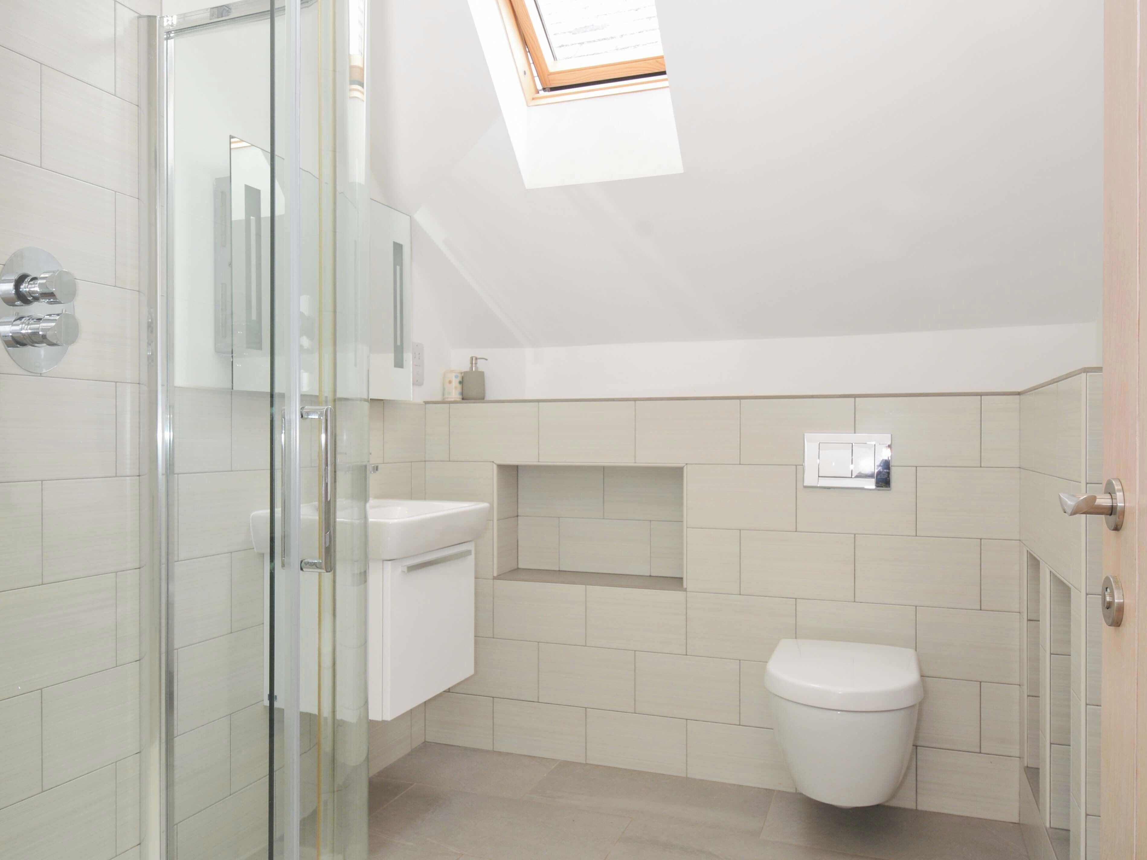 Et moderne badeværelse med brusekabine i glas, toilet og et lille vindue over vasken.