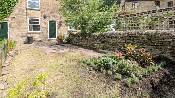 Une maison en pierre avec une porte verte, une cheminée en briques et un jardin où poussent différentes espèces de plantes.