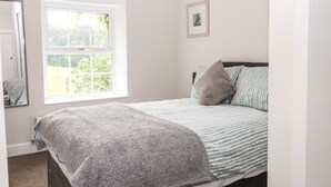 Une chambre à coucher avec un lit, une fenêtre, un miroir et un tableau encadré accroché au mur.
