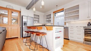 Una cocina moderna con armarios blancos, una isla central con taburetes, un refrigerador de acero inoxidable y un horno empotrado.