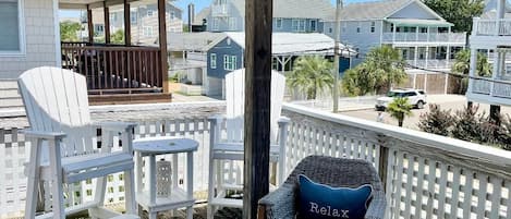 Terraza techada al aire libre con sillas blancas y una mesa de madera, con vista a una zona residencial.