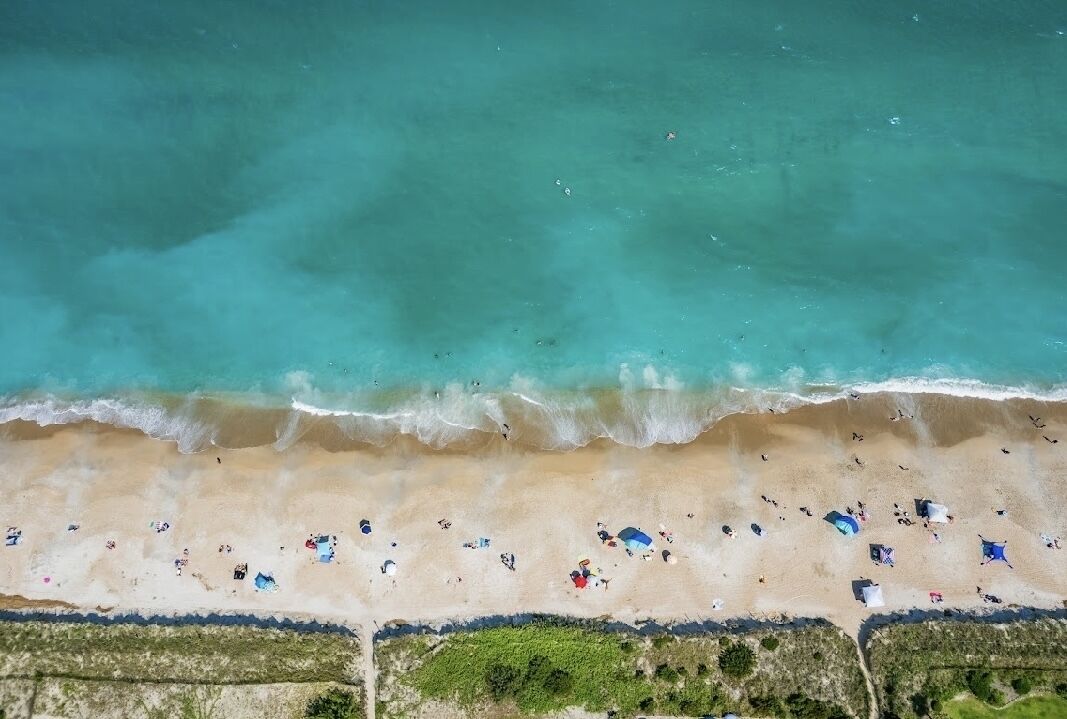 An aerial view of a beach with clear turquoise water, sandy shore, and scattered beach umbrellas.