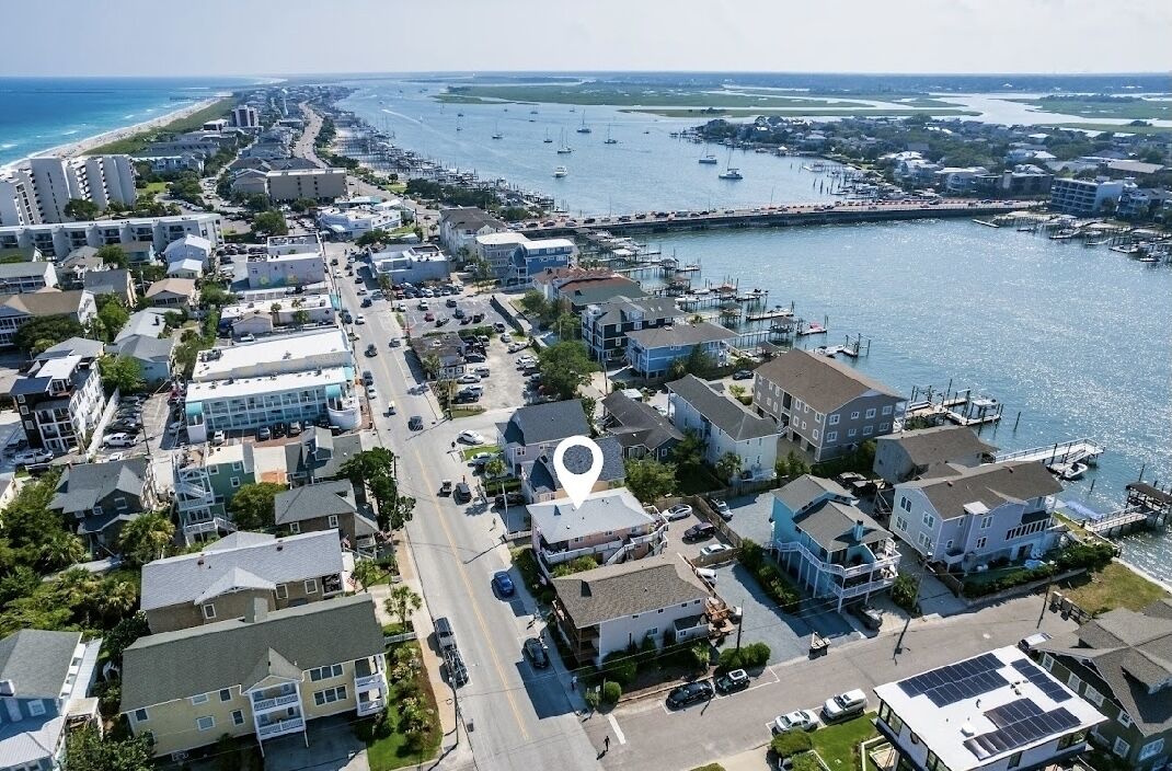 An aerial view of a coastal town with a marina, residential buildings, and a road leading to the beach.