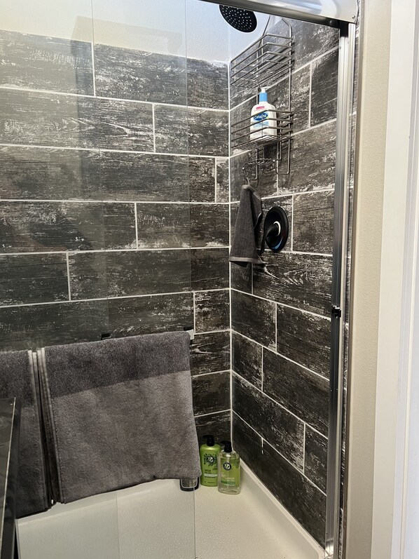 Une douche aux carreaux noirs, une serviette et deux flacons verts de shampoing et d’après-shampoing.