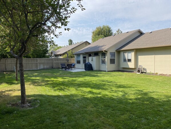 A residential backyard with a lawn, a tree, a barbecue area, and a house with a sloped roof.