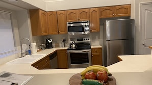 A kitchen with wooden cabinets, stainless steel appliances, a sink, and a countertop with a plate of fruit and packaged snacks. - Just like home, clean in great family friendly location (Boise)