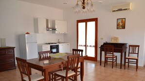 Un comedor con mesa y sillas de madera, una cocina con armarios blancos y un ventanal con cortinas.