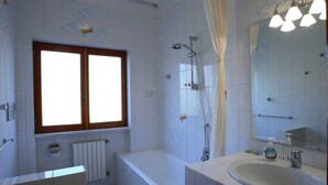 Un baño con bañera, ducha, lavamanos y ventana.