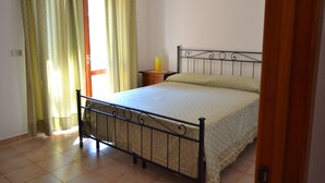 Un dormitorio con cama, cortinas, mesita de noche y una puerta.