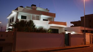 Un edificio residencial moderno de varios pisos con techo plano, ventanas amplias y entrada protegida por una reja.