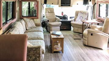 Un interior de caravana acogedor con sofá, sillas, una mesita y chimenea.