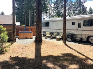 A recreational vehicle (RV) parked in a wooded area with a hot tub and outdoor seating.