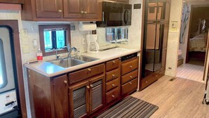 A compact kitchen with wooden cabinets, a microwave, a coffee maker, and a dishwasher. - The Great Escape - Shirley (Sooke)